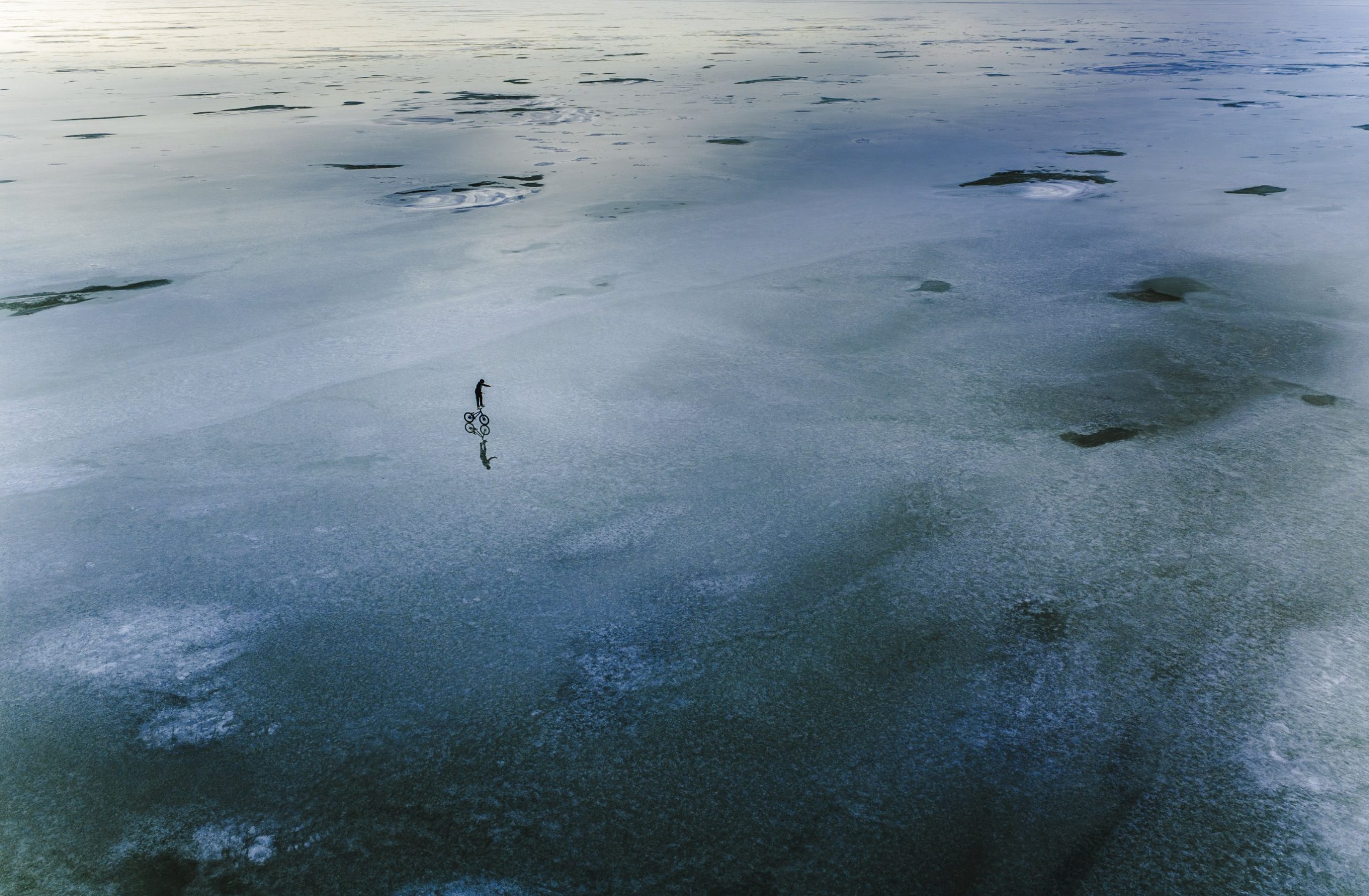 Aerial view of a rider balancing on a bike on a frozen lake at dusk
