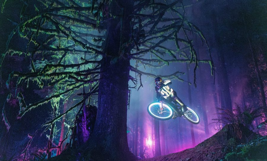 Hannah Bergemann jumping a mountain bike at night through a neon-lit forest in Lear Miller's Illume Awards 2026 Bike Category winning photo